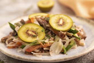 Meat salad with beef kiwi and vegetables on brown concrete background and orange linen textile.