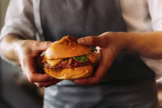 Close-up of an artisan burger presented by a chef. Brioche bun, juicy beef, and melted cheese take