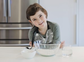 A young child in an apron is smiling while preparing to bake in a modern kitchen. The scene