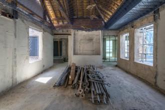 A spacious room in an unfinished building shows construction materials on the floor, open windows,