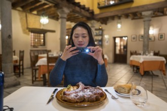 An Asian woman captures a photo of an Avila T-bone steak before dining in a restaurant with a warm