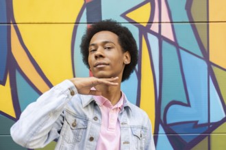 A confident non-binary person stands proudly in front of a vibrant graffiti mural. They wear a