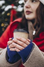 A young woman wearing a white beanie and a red scarf is captured holding a coffee cup on a chilly