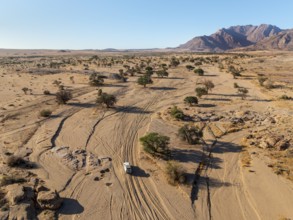 Aerial view of off-road car driving in dry riverbed and desert landscape on the Ugab River, behind
