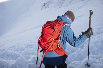 A skier with a red backpack explores a winter landscape during a ski touring adventure. The