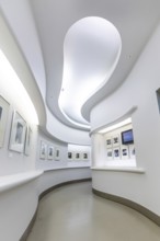 Bright, minimalist exhibition space with undulating white walls and artworks on the walls, Berlin,