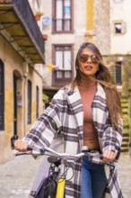 Pretty latin woman with sunglasses doing bicycle sightseeing in the city through the old town.