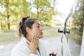 A woman enjoys her skincare routine while experiencing the freedom of van life in autumn. Captured