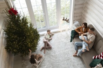 A family celebrates Christmas in a cozy room adorned with a large, lit Christmas tree. A couple