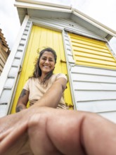 A woman smiles while leaning against a brightly painted yellow Brighton Bathing Box in Melbourne,