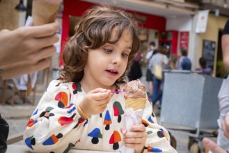 A young girl delights in eating chocolate ice cream from a cone in a quaint village scene,
