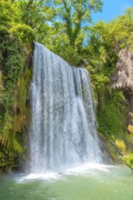 A waterfall is flowing into a pool of water. The water is clear and the sky is blue