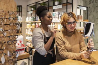 Two women in a cosmetics store engage in a friendly interaction. One is holding a mirror, while the