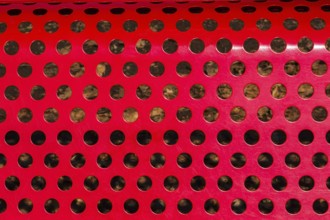 Close-up of vibrant red painted metal sitting bench backrest with perforated round holes, Quebec,