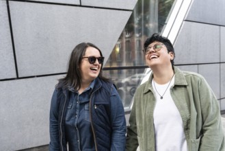 A happy lesbian couple enjoying a sunny day, laughing together outdoors in an urban setting. They