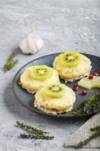 Pieces of baked pork with pineapple, cheese and kiwi on gray background, side view, close up