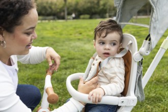 A loving mother bends down to interact with her baby sitting in a stroller. They are enjoying a
