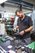 Vertical photo of an adult caucasian male worker using micrometer to measure metal pieces in cnc