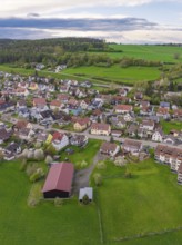 Overview of a village with scattered houses and large green spaces, surrounded by forests,