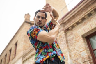 A male dancer in a vibrant, patterned shirt strikes a dynamic pose against a brick building