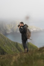 A photographer with a backpack captures the beauty of Norway's coastal cliffs, surrounded by lush