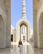 A woman wearing an headscarf walks through the grand architecture of the Sultan Qaboos Mosque in