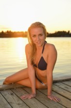 Woman in a bikini sitting on a dock by the water at sunset, Austria