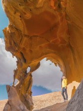 A woman in a bright yellow jacket explores a striking natural rock arch in a desert landscape of