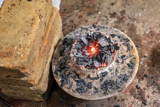 Close-up of a fire pit with embers and coals on metal plate with bricks piled next to it, a kiln