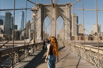 A woman with long hair walks on the iconic Brooklyn Bridge in New York City, capturing the stunning