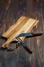 Shabby wooden table with empty cutting board and old forged knife and fork for barbecue