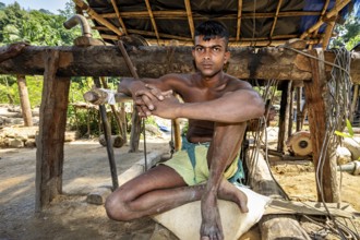 A young man sits relaxed in a rustic outdoor wooden structure, the sapphire and gemstone mines at