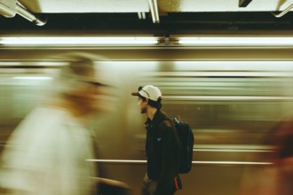 A man pauses in a bustling subway, surrounded by blurred commuters in New York. The scene captures