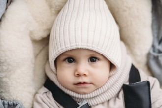 A young child in cozy autumn attire gazes with curiosity. The child wears a knitted hat and