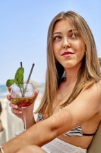 A young woman relaxes at the beach, enjoying a colorful cocktail while soaking up the sun. The