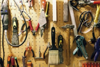 Pegboard displaying assorted luthier tools for crafting bass guitars, including pliers, brushes,