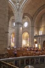 Interior view of a church with high walls and visitors in rows of seats, Paris