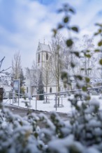 Snow-covered church with decorated tower behind trees and bushes, Aidlingen, Böblingen district,