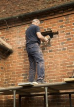 Builder removing red bricks to make window space, Suffolk, England, UK