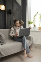 A mother working on a laptop at home with her young child lovingly embracing her. A cozy, modern
