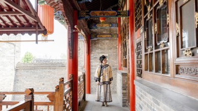 A young woman dressed in traditional Qing Dynasty attire stands gracefully in a historic corridor