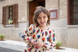 A joyful child, dressed in colorful attire, plays in the sunlit street of a quaint village,