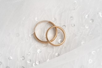 Close-up of two intertwined rose gold wedding rings atop a delicate white lace fabric, symbolizing
