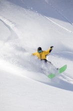 A snowboarder in a vibrant yellow jacket expertly carves through fresh powder on a snowy mountain