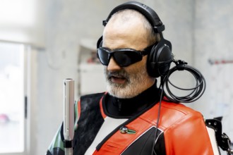 A blind marksman, wearing headphones and protective gear, concentrates during training. The image