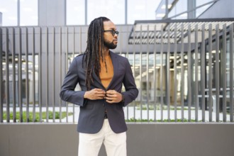 A cuban business man in a dark blazer and sunglasses stands confidently against a contemporary