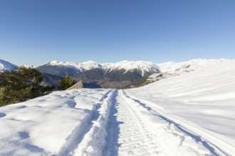 A pristine snowmobile trail cuts through a winter wonderland, with towering snow-covered mountains