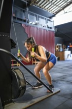 Vertical photo of a Chinese strong woman bending while pulling weights with a lat machine in a