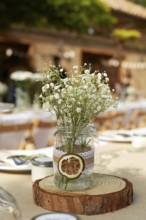 A rustic wedding table centerpiece featuring delicate white flowers in a mason jar adorned with
