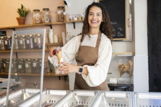 A cheerful woman working in an ice cream shop, serving a scoop of delicious ice cream in a cone.